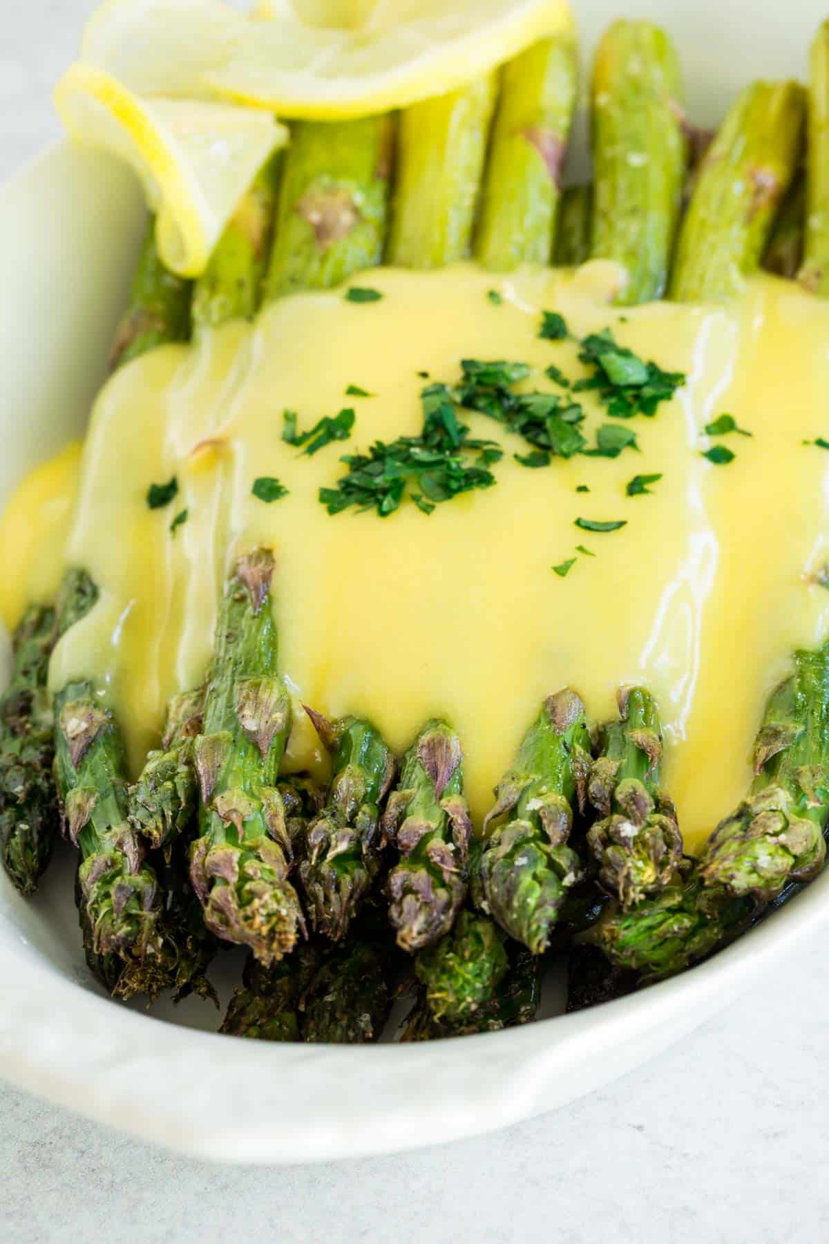 Close up of roasted asparagus with hollandaise in a white serving dish.