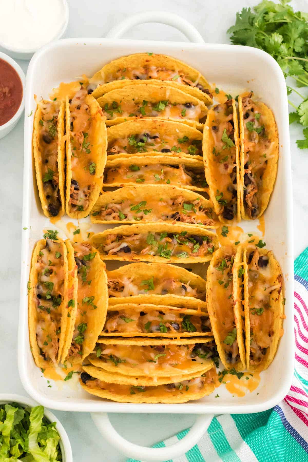 Top view of baked chicken tacos in a white baking dish surrounded by toppings.