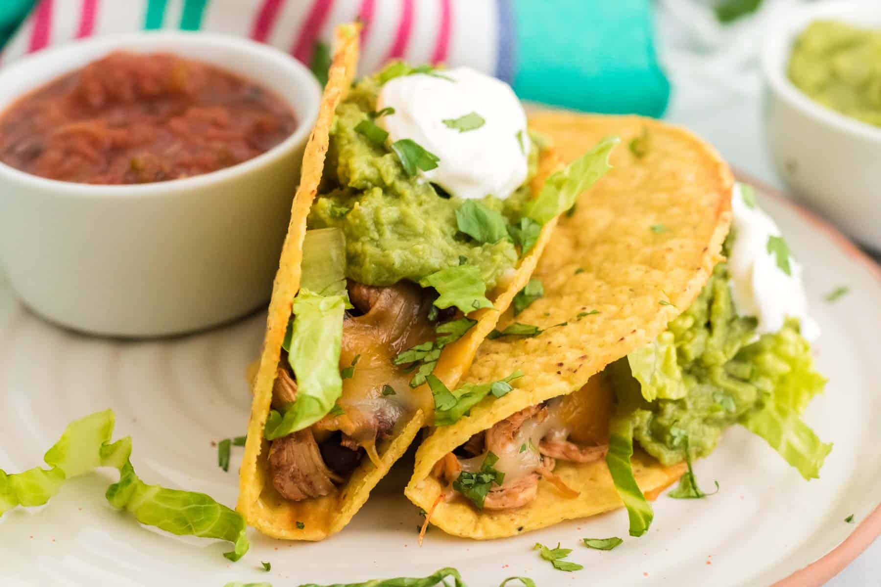 Two chicken tacos on a plate with a bowl of salsa.