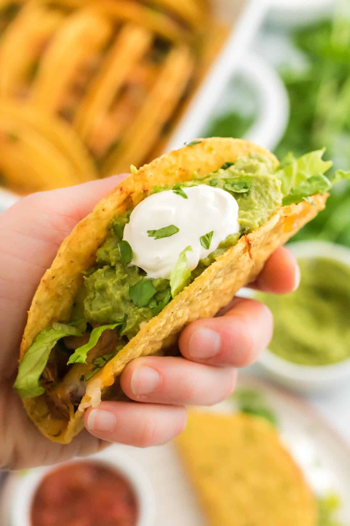 A hand holding a chicken taco filled with toppings and sour cream.