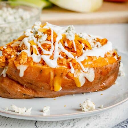 A buffalo chicken sweet potato on a plate topped with blue cheese and Ranch.