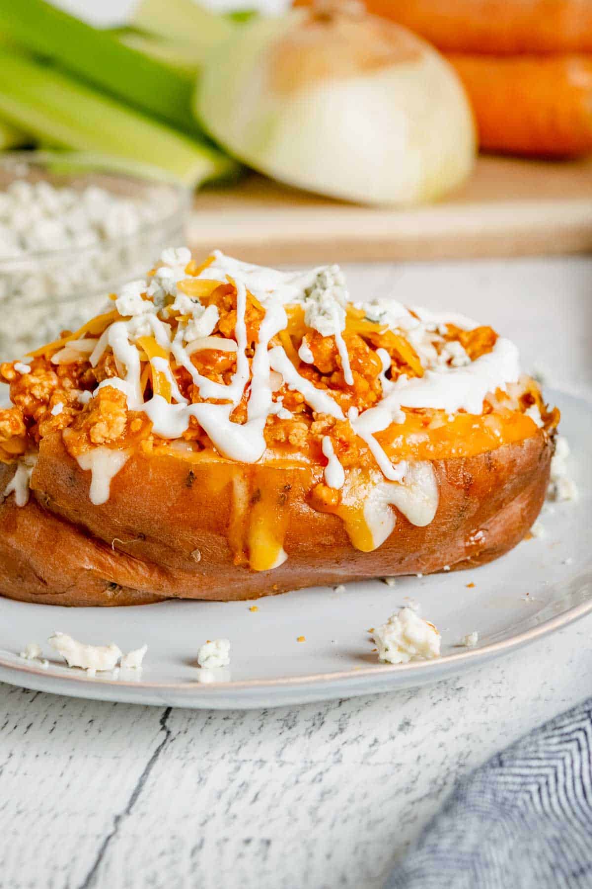 A buffalo chicken sweet potato on a plate topped with blue cheese and Ranch.