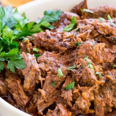 Crockpot barbecue beef in a white bowl garnished with fresh parsley.