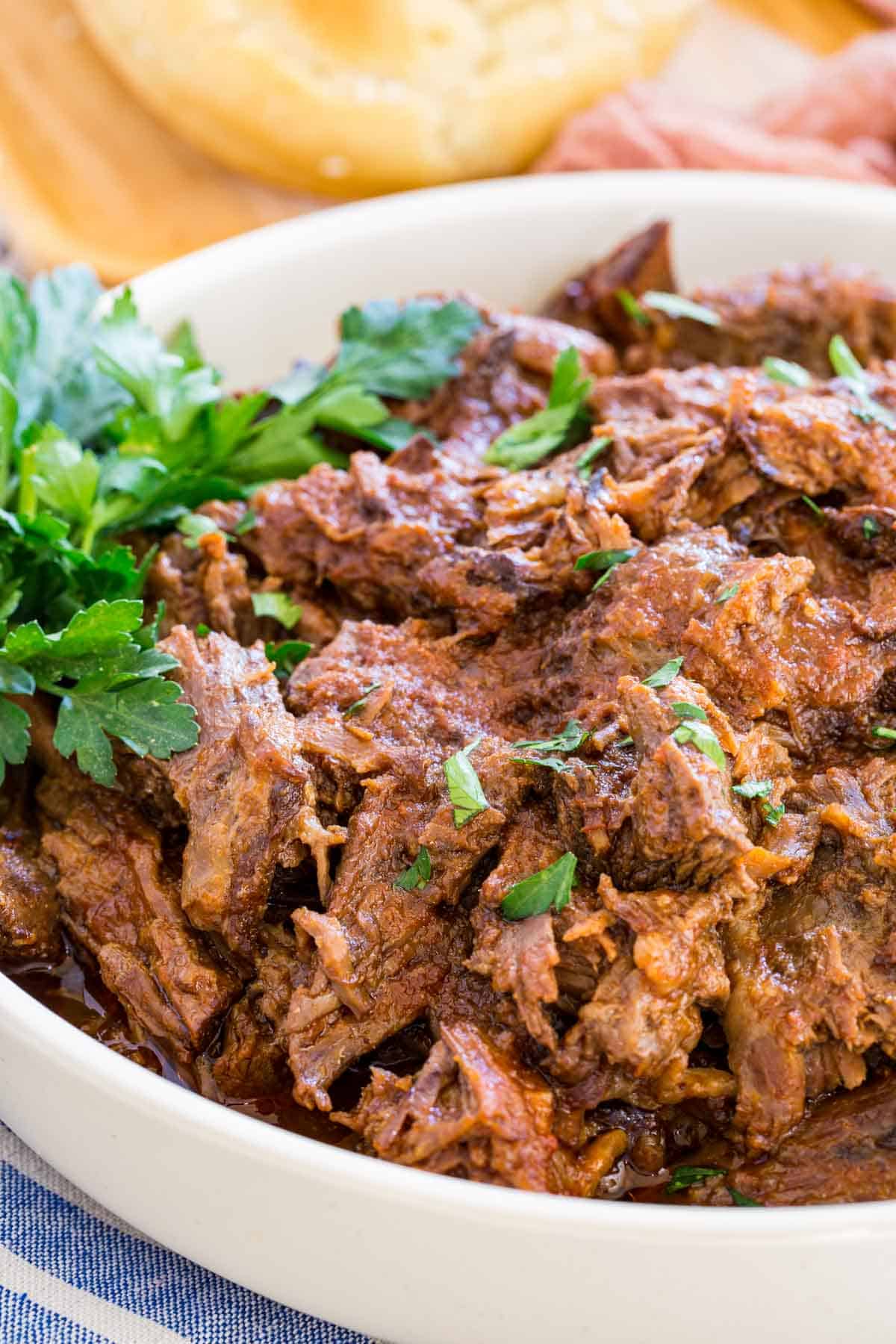 Crockpot barbecue beef in a white bowl garnished with fresh parsley.