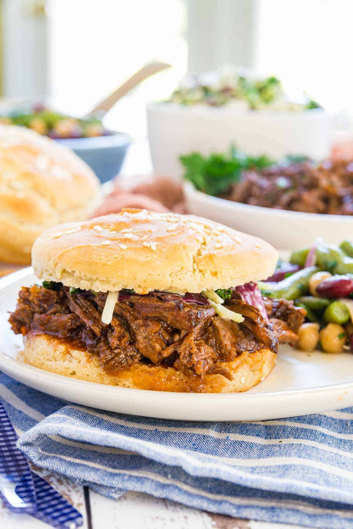 A Crockpot barbecue beef sandwich served on a plate with three bean salad.