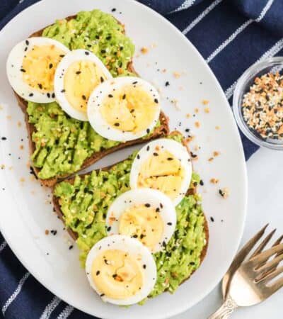 Two slices of gluten-free avocado toast topped with sliced hard boiled eggs on a white plate.