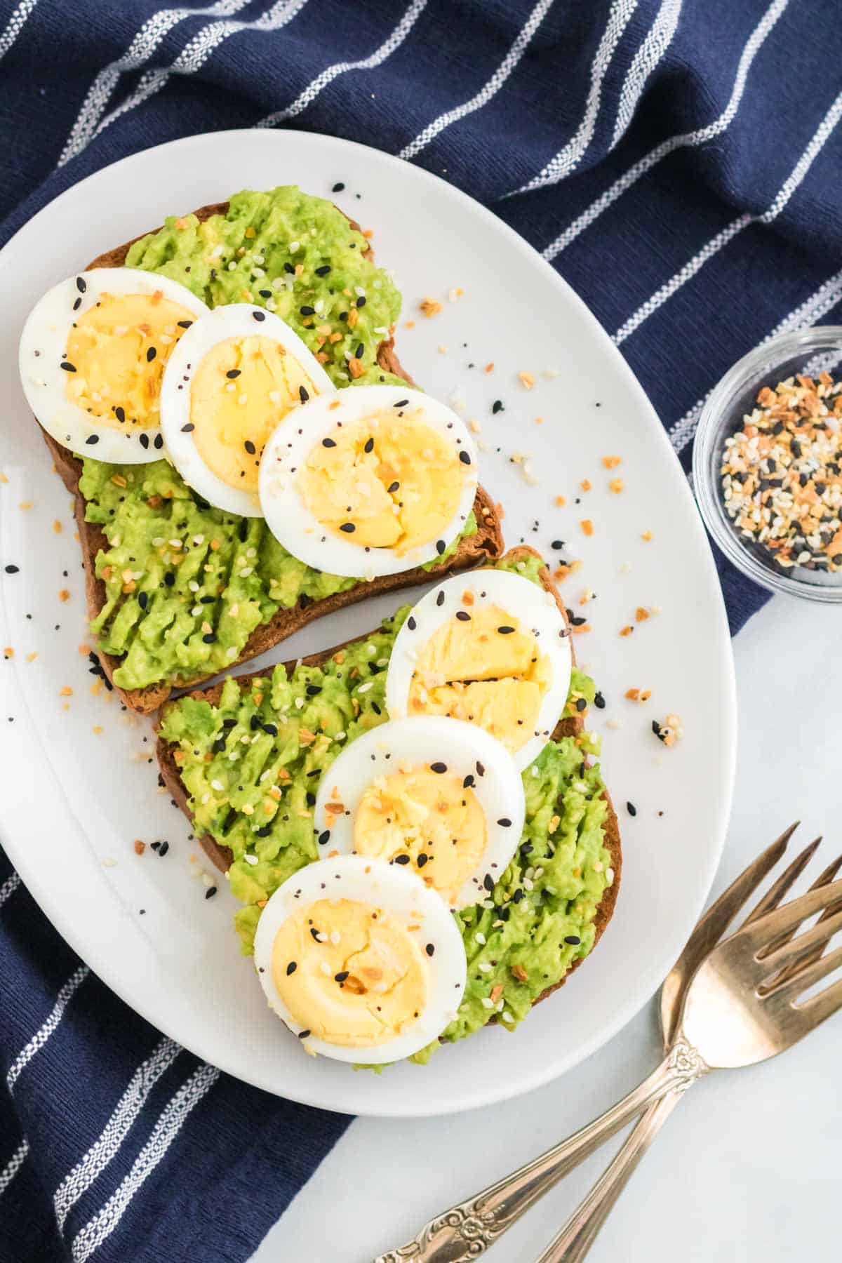 Two slices of gluten-free avocado toast topped with sliced hard boiled eggs on a white plate.