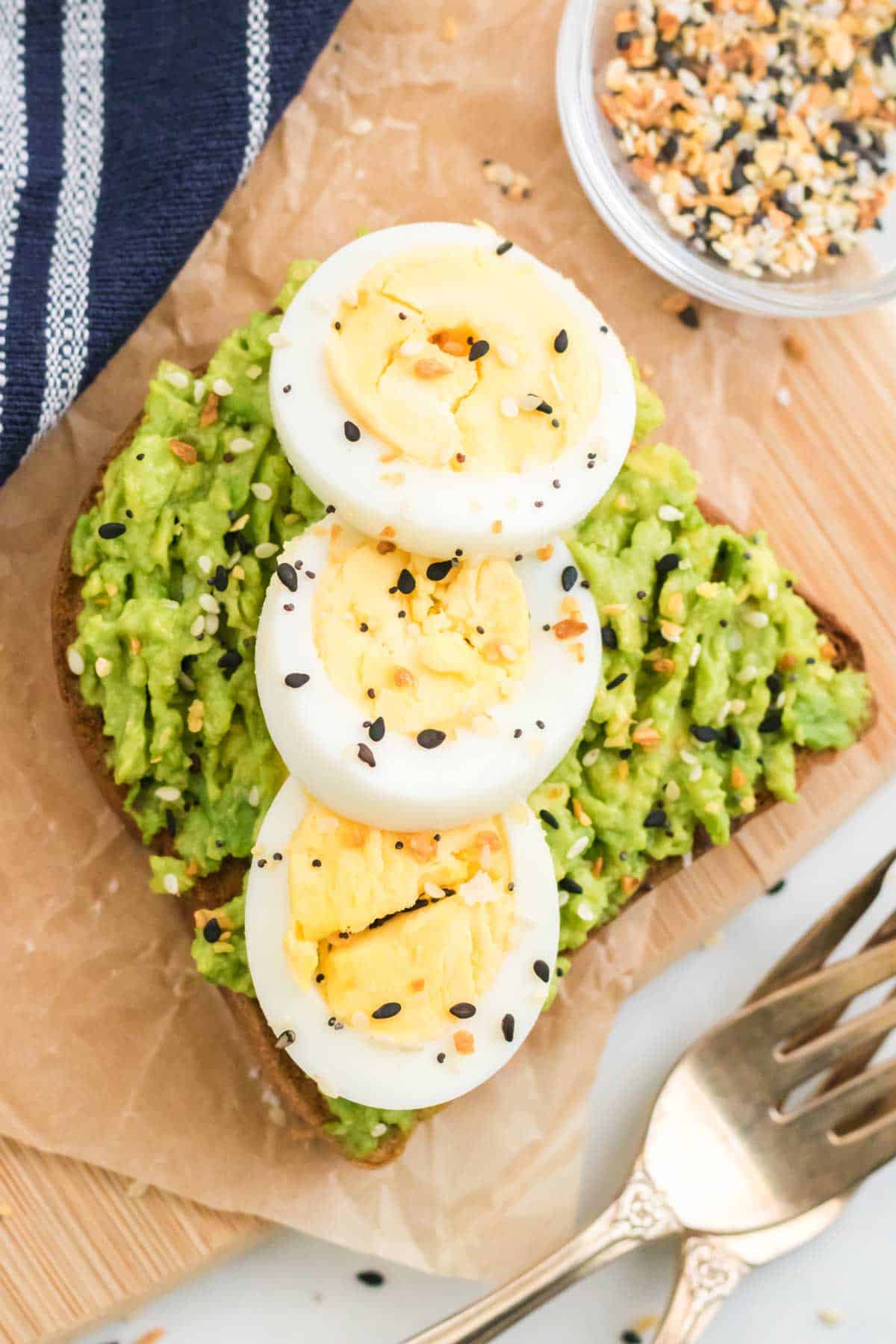 Avocado toast topped with sliced eggs and seasoning next to a fork.