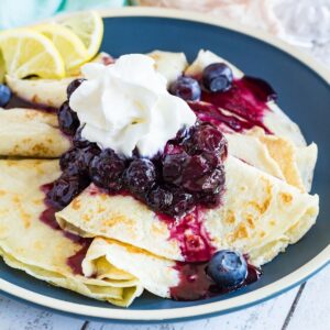 Homemade crepes topped blueberry syrup and whipped cream with a few fresh berries on the plate.