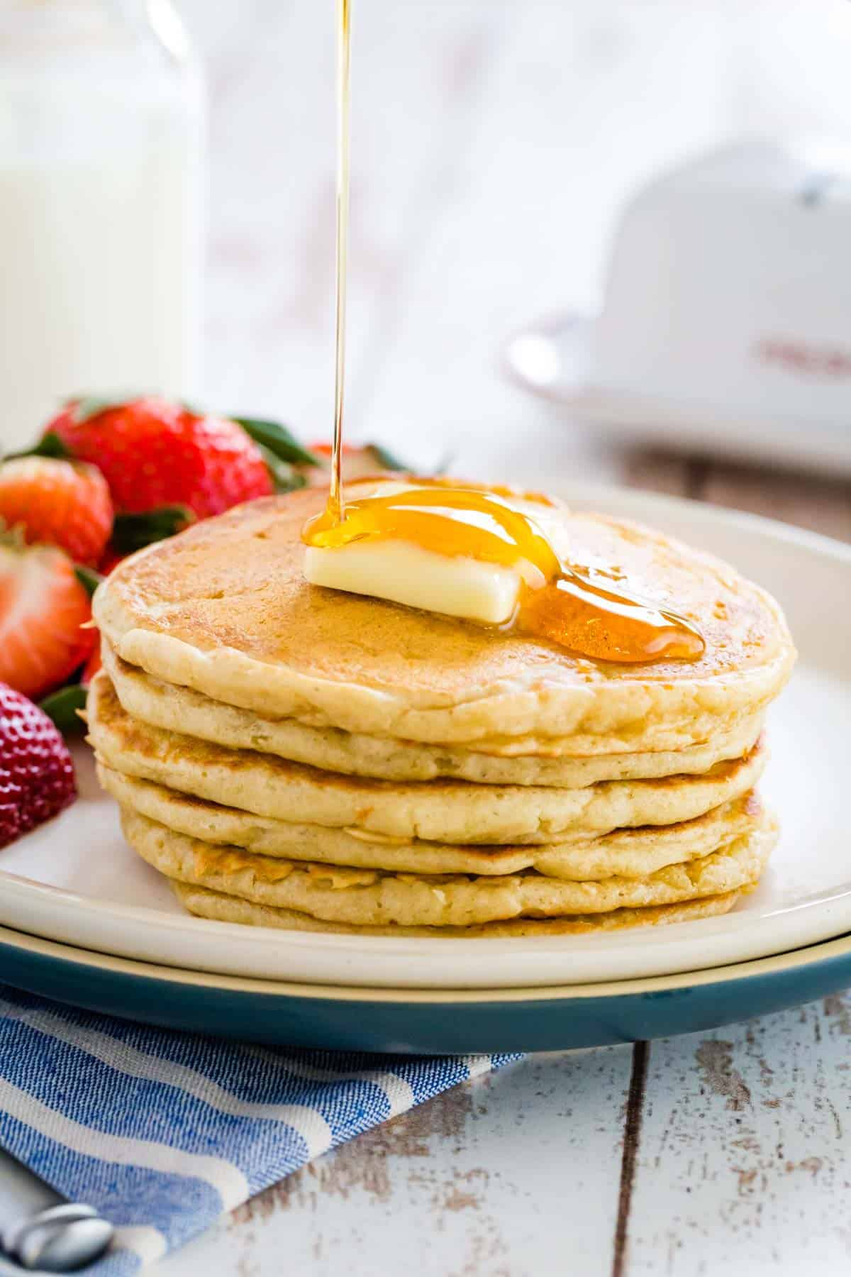 A stack of gluten free buttermilk pancakes topped with a slab of butter and maple syrup.