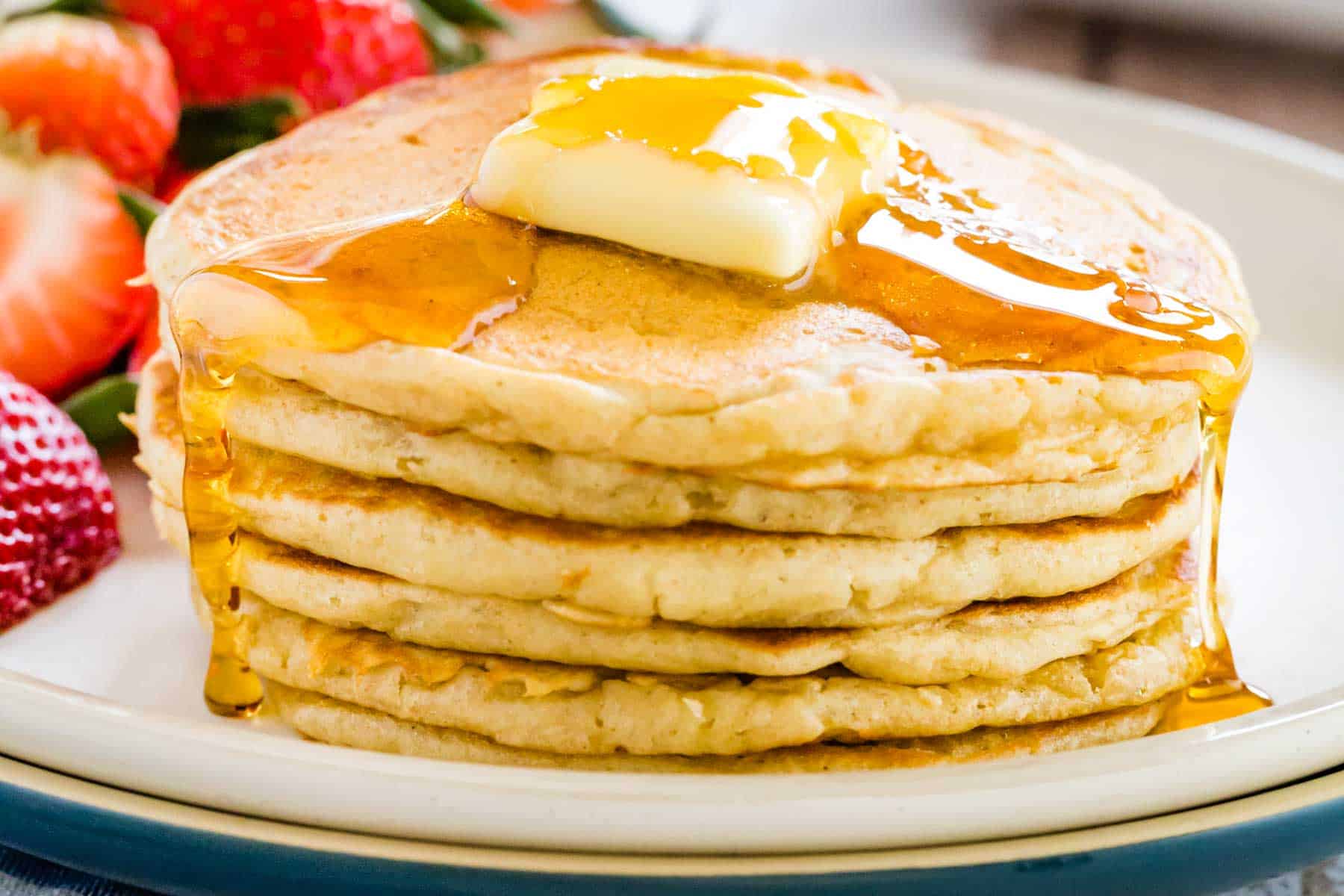 A stack of gluten free buttermilk pancakes topped with a slab of butter and maple syrup.