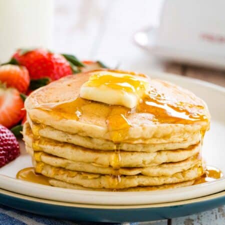 A stack of gluten free buttermilk pancakes topped with a slab of butter and maple syrup.