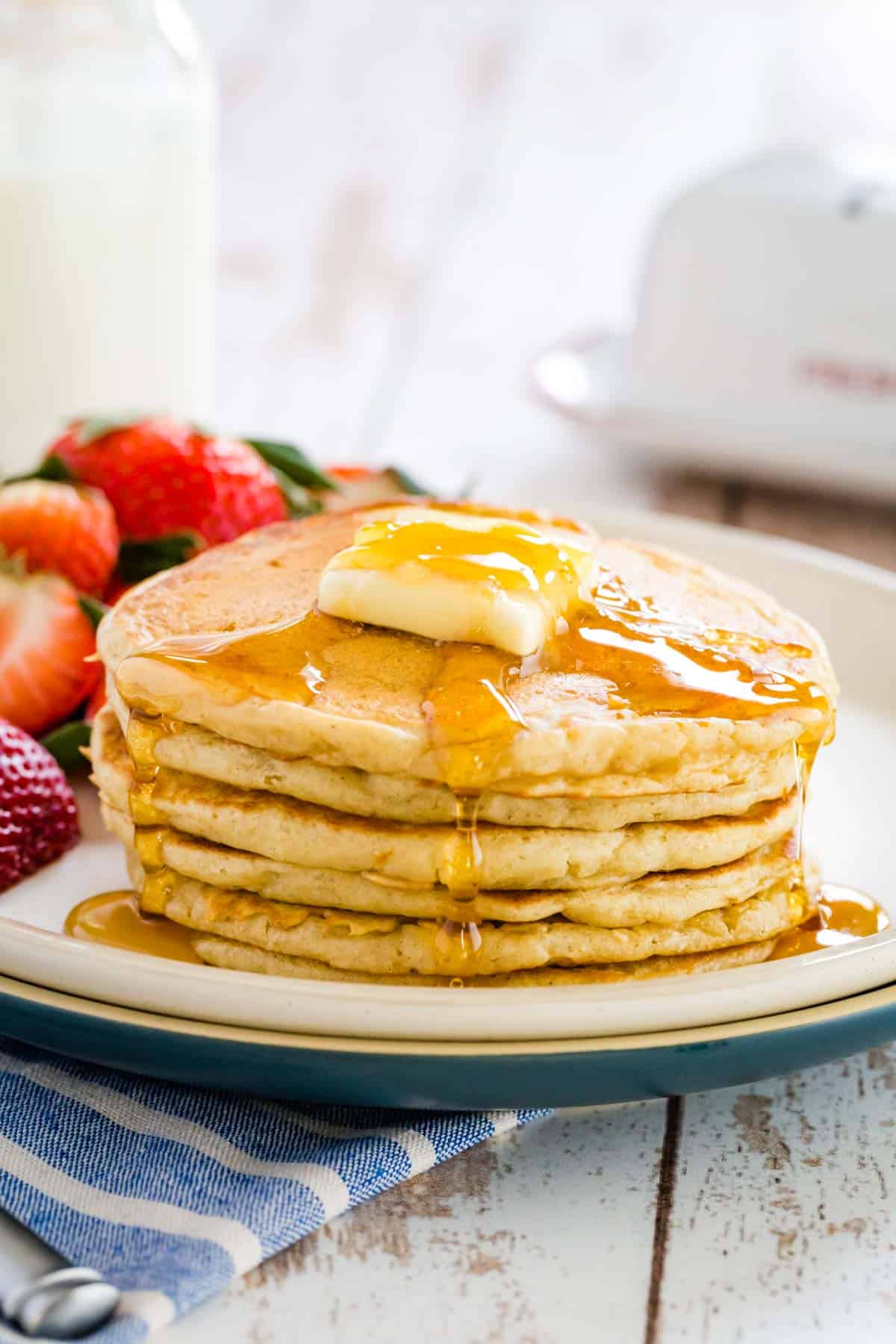A stack of gluten free buttermilk pancakes topped with a slab of butter and maple syrup.