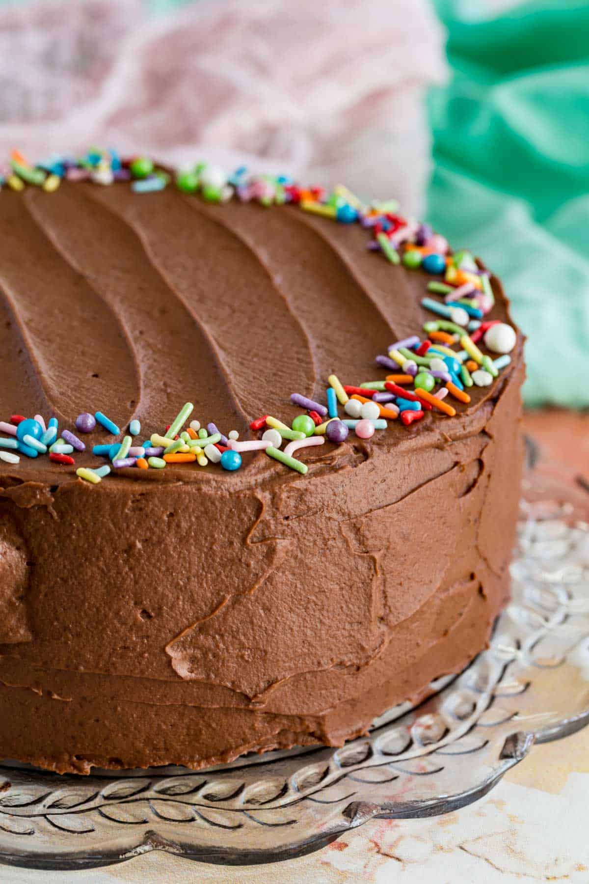 A whole frosted gluten-free chocolate layer cake decorated with rainbow sprinkles.