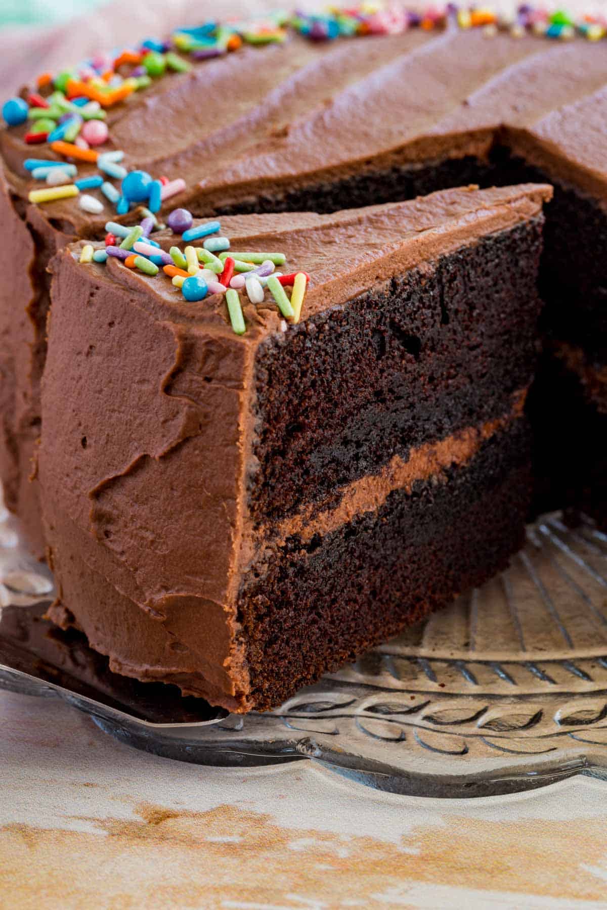 A slice of gluten-free chocolate layer cake being served from the full cake.