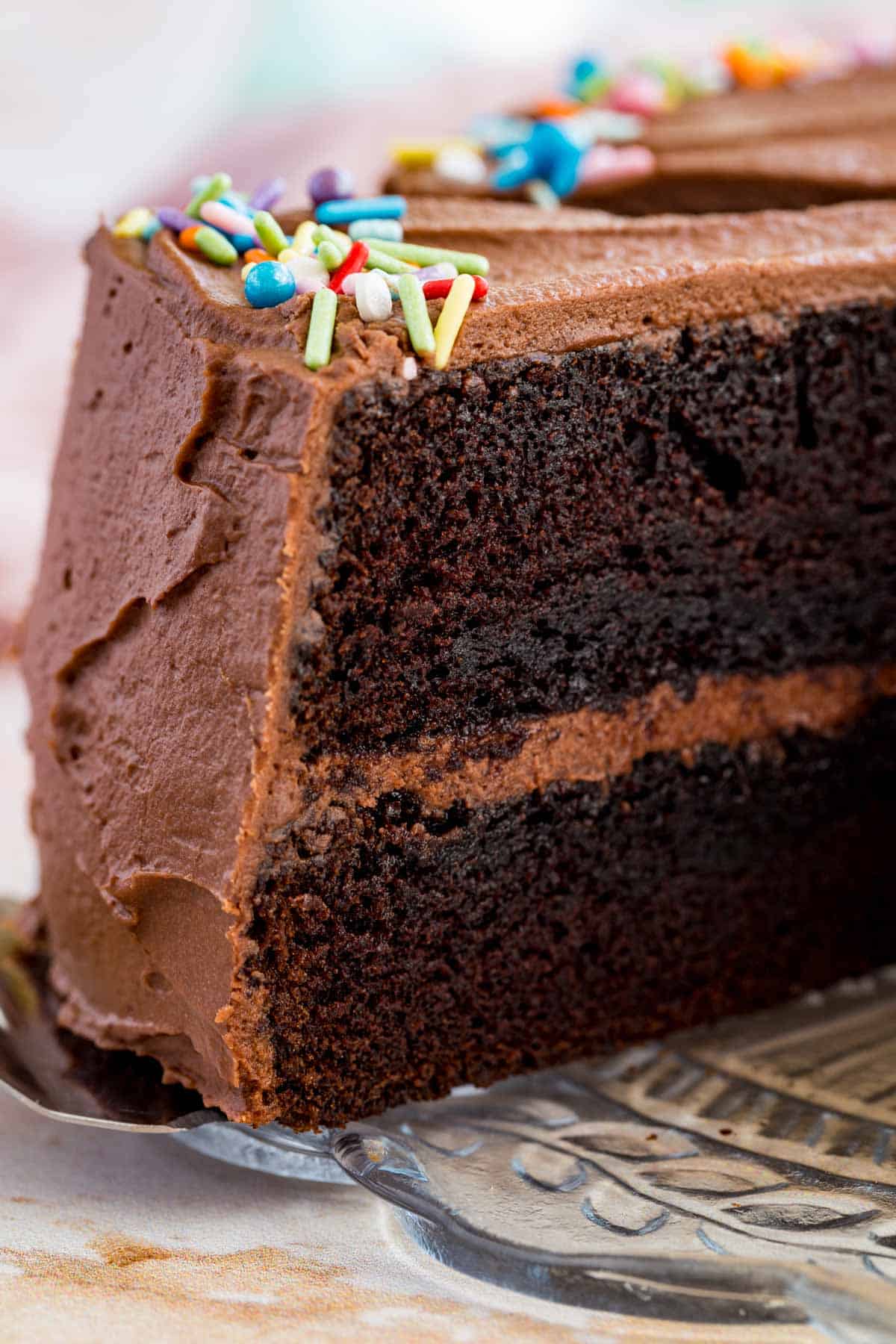 Close up of a slice of gluten-free chocolate layer cake being served from the full cake.