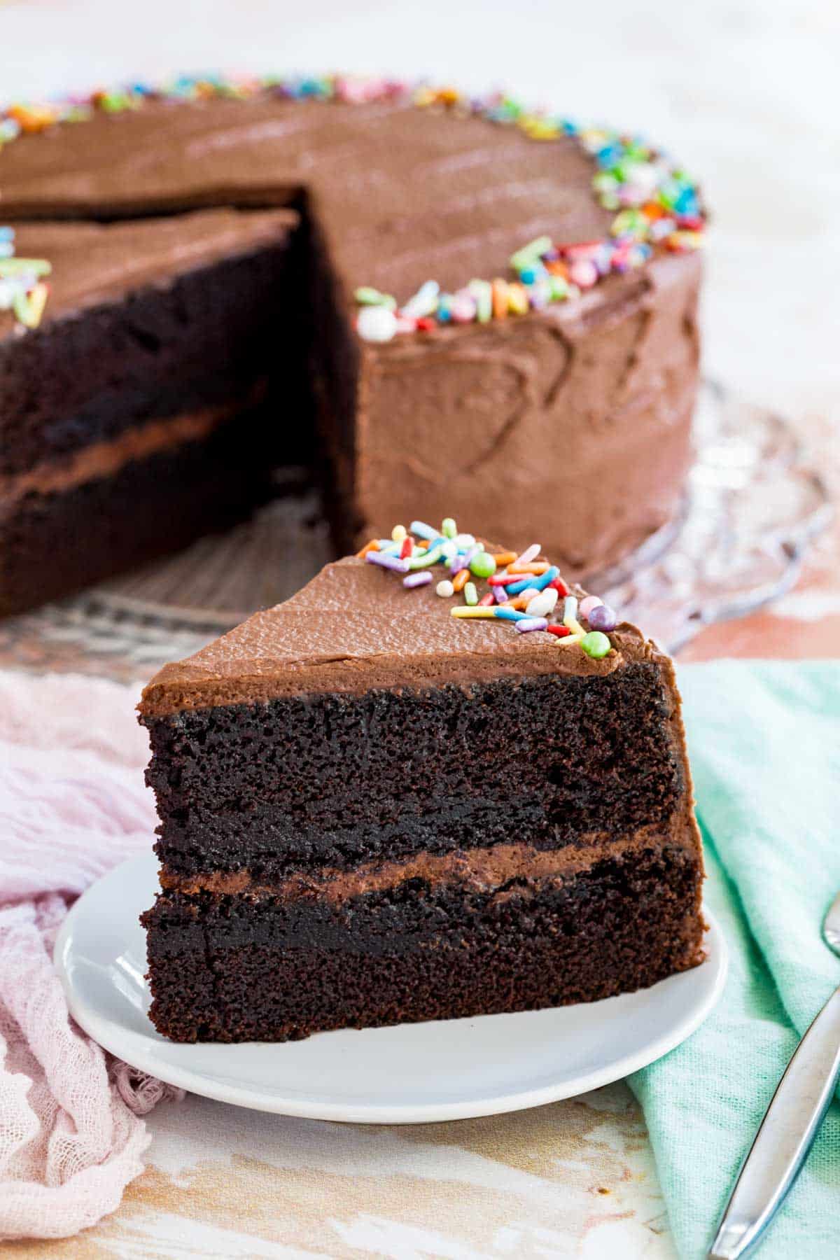 A slice of gluten-free chocolate layer cake on a plate next to the full cake.