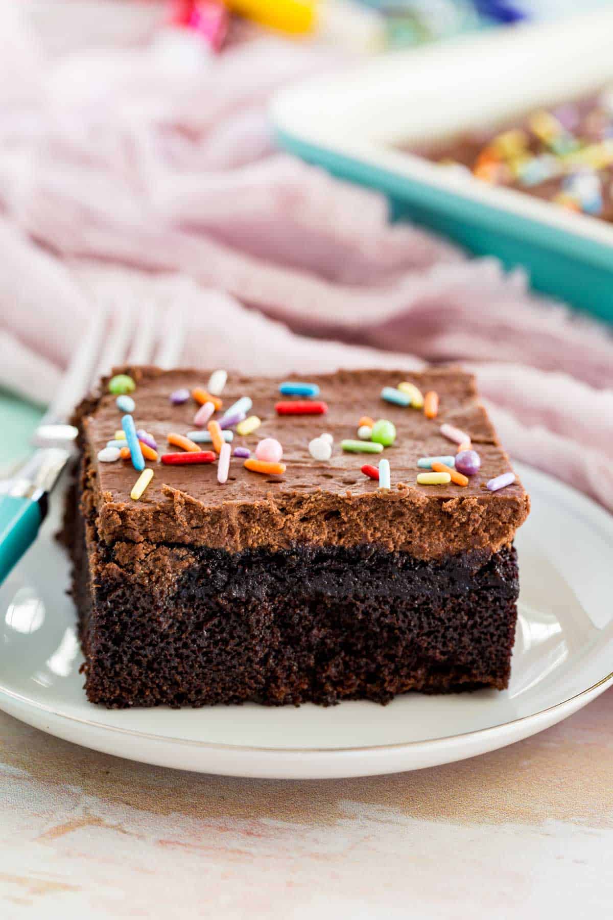 A square slice of chocolate cake with sprinkles on a plate.
