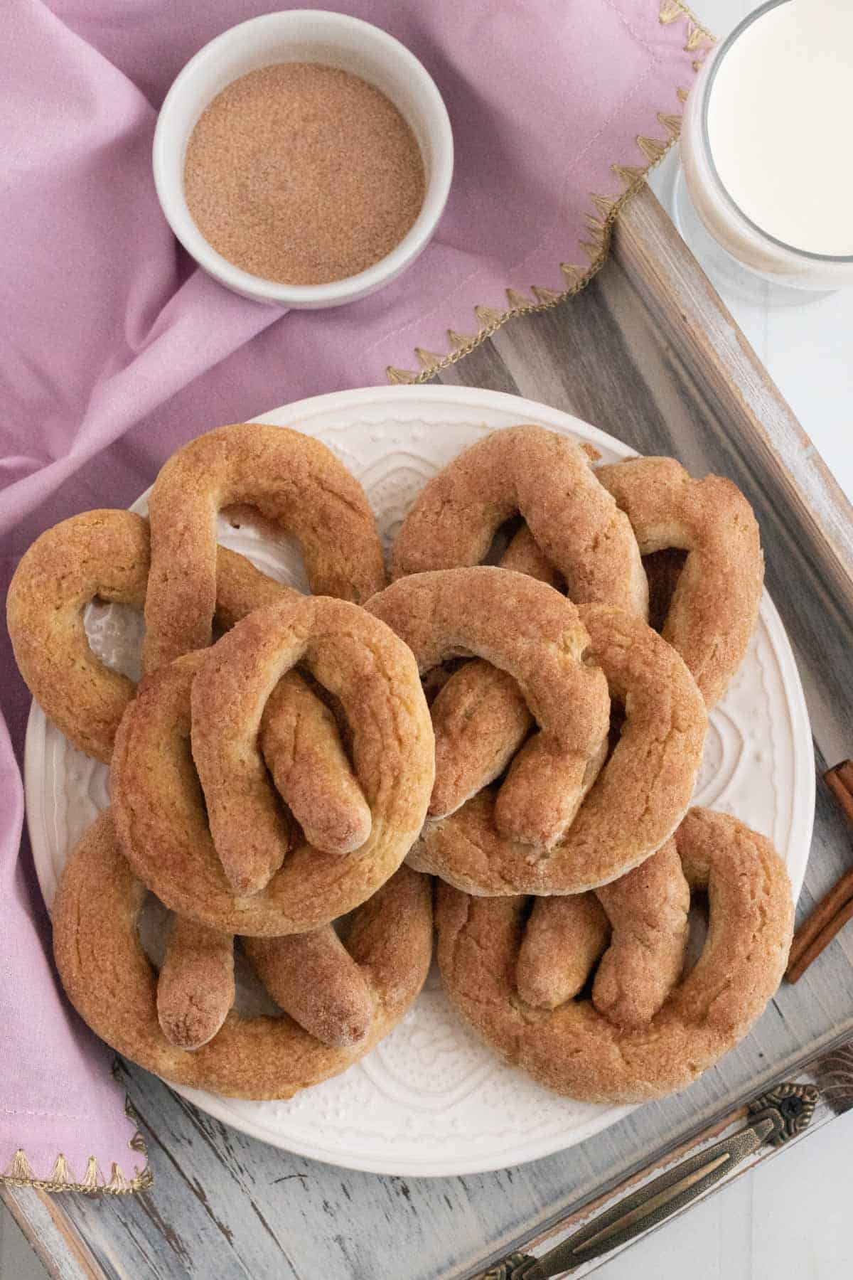 A plate of cinnamon sugar pretzels on a wooden tray with a bowl of cinnamon sugar.