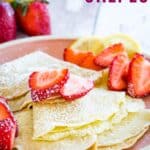 Folded crepes on a pink plate with strawberry slices and powdered sugar on top.