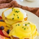 Two eggs benedict with fresh strawberries, blueberries, and orange segments.