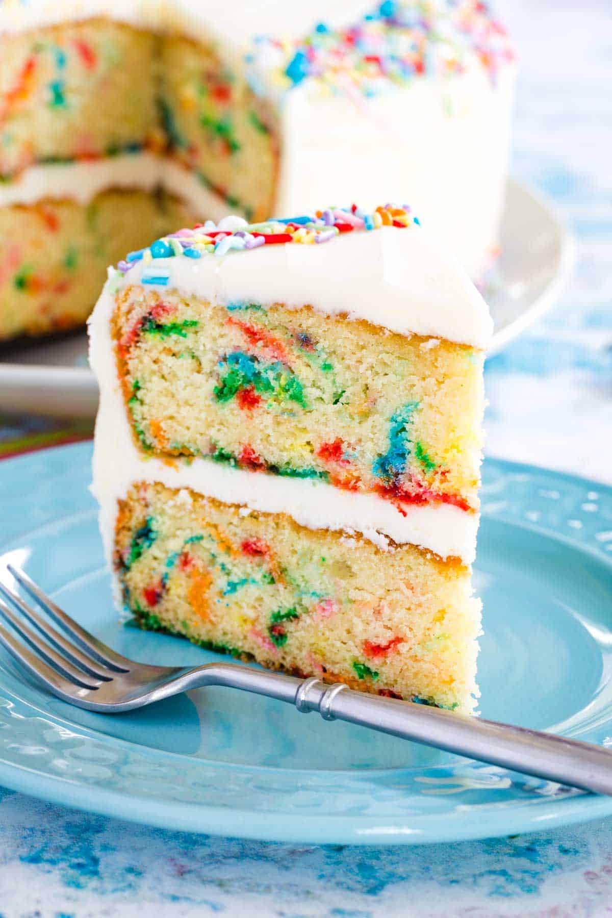 A slice of gluten free funfetti cake on a blue plate next to a fork.