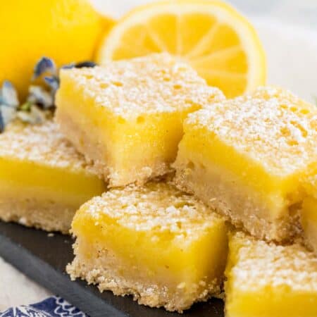 A stack of gluten free lemon bars on a rectangular platter with lemons in the background.