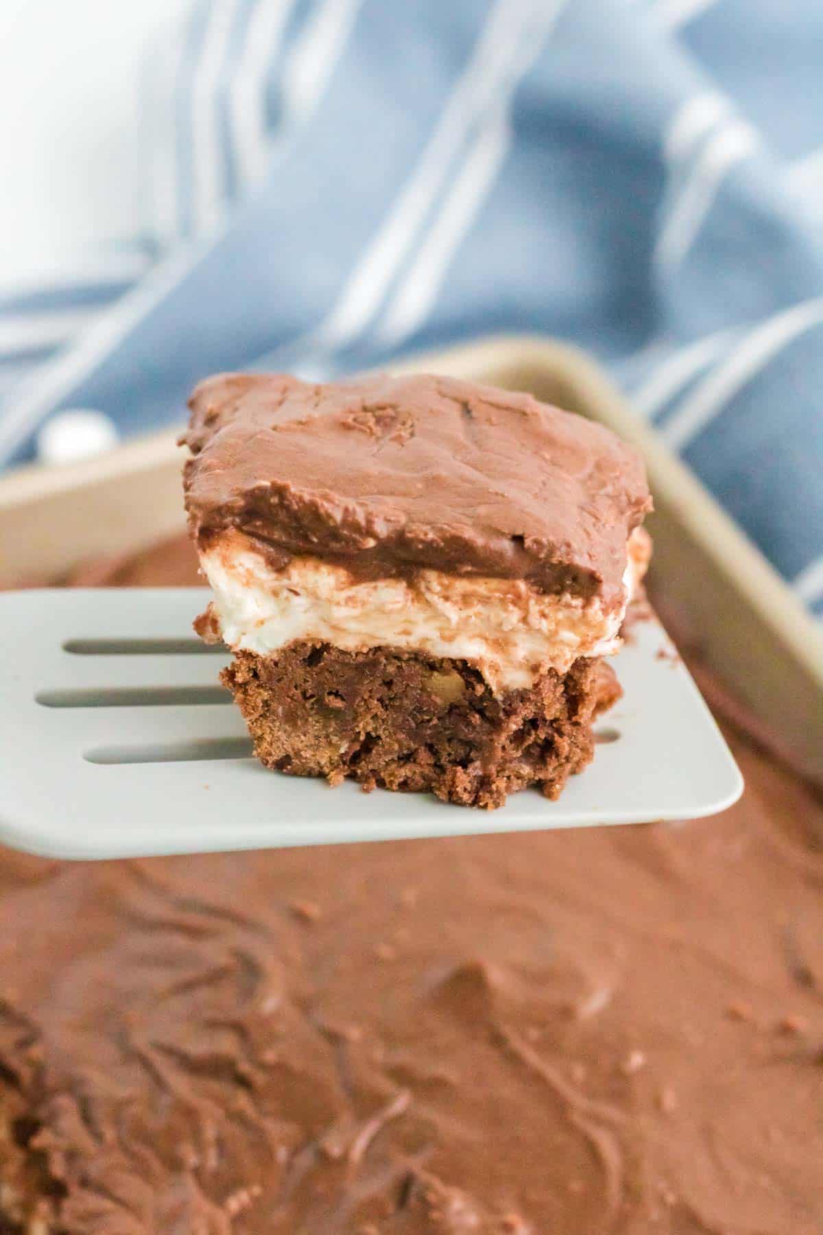 A frosted walnut brownie with a layer of marshmallow being picked up on a spatula.