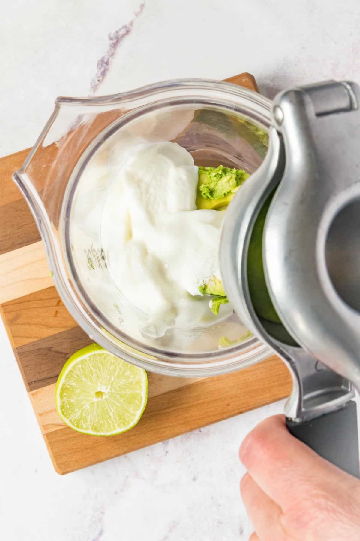 Squeezing a lime with a juicer into a small blender jar with avocado and Greek yogurt.