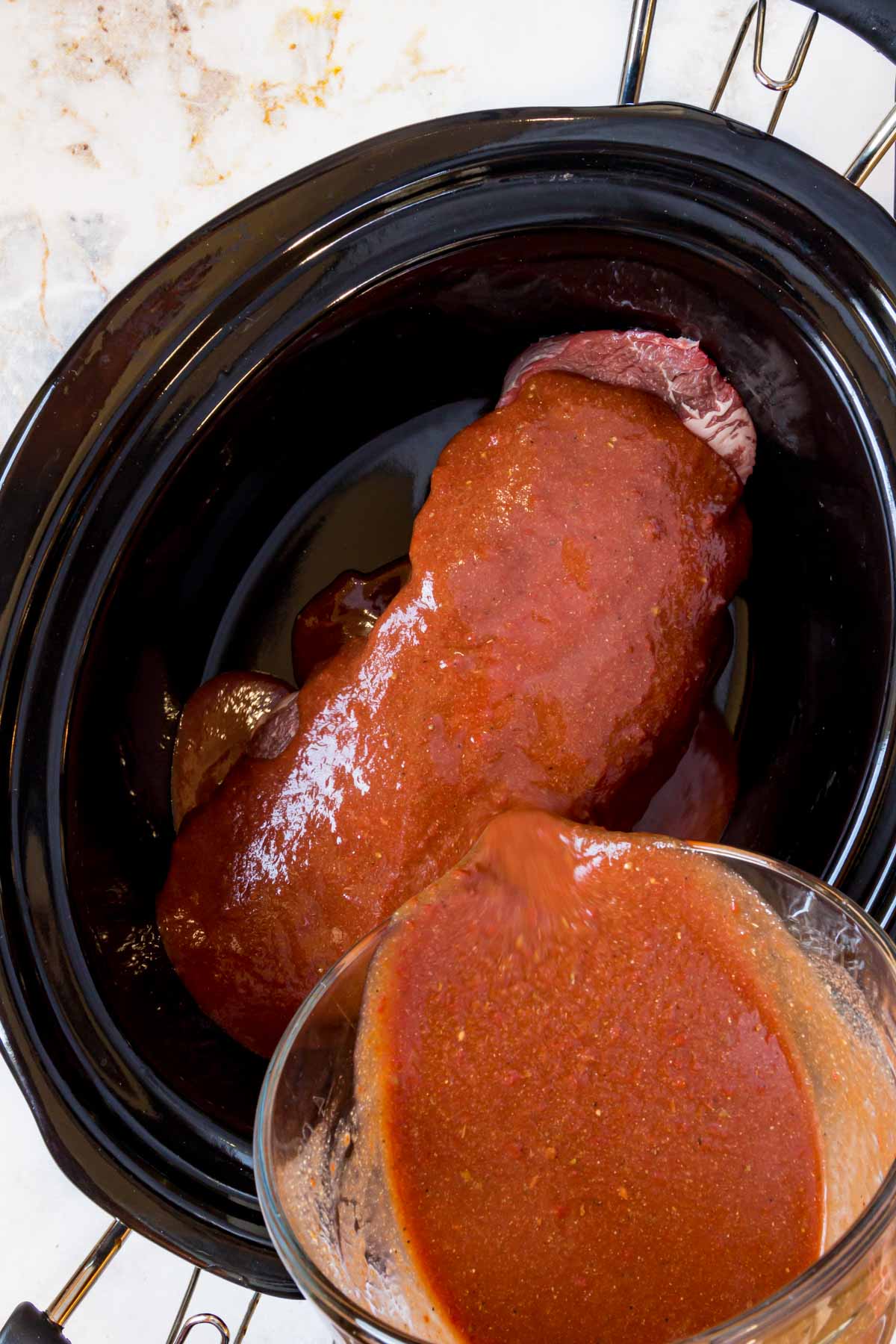 BBQ sauce is poured over beef chuck roast in the bowl of a crockpot.