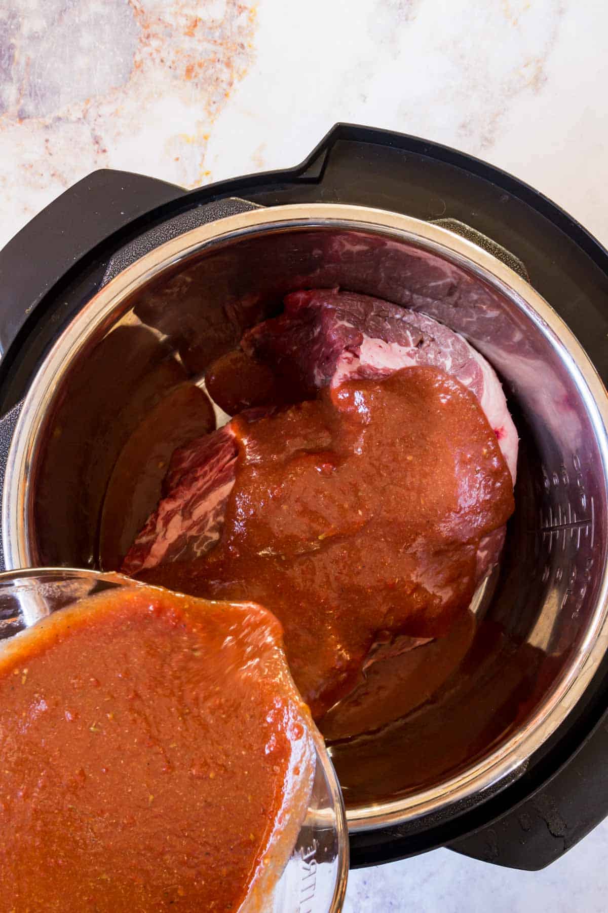 BBQ sauce is poured over beef chuck roast in the bowl of an Instant Pot.