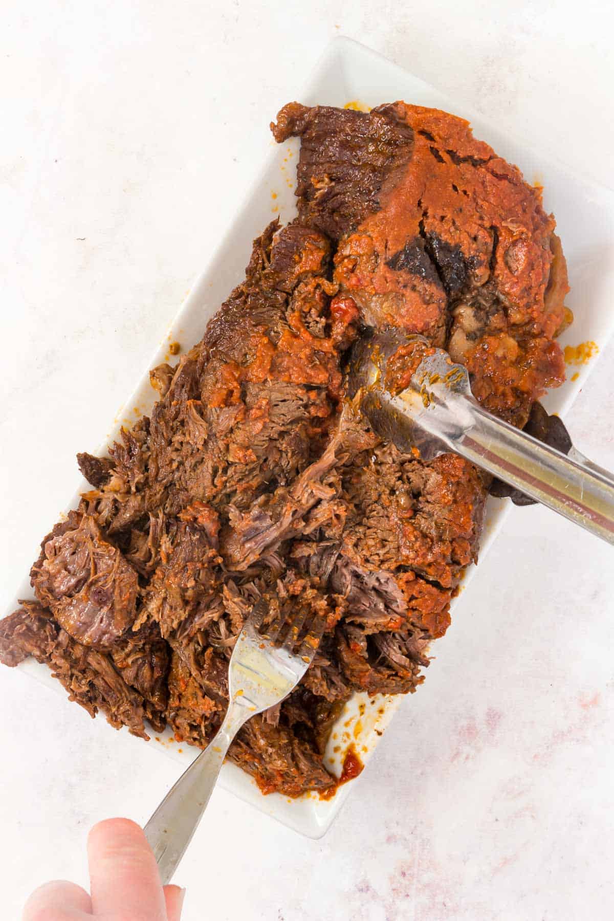 A fork and knife is used to shred a slow cooked barbecue beef chuck roast.