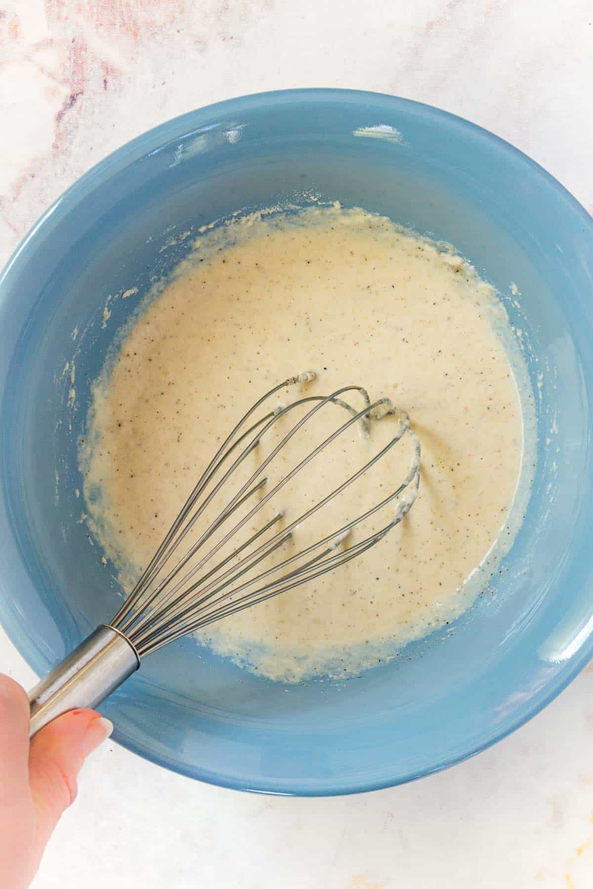 Hand holding a whisk in a bowl of batter.