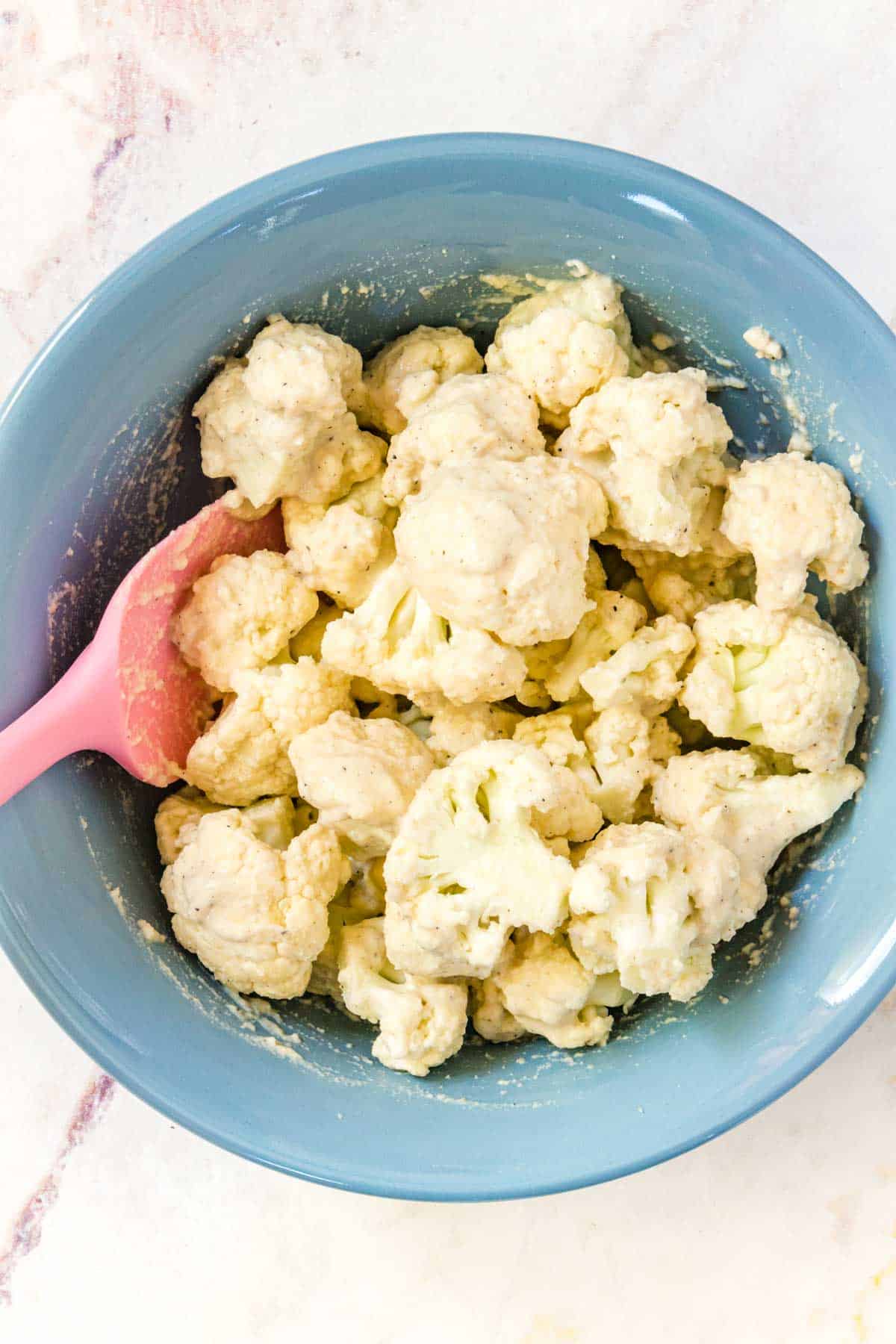 Cauliflower florets being coated in batter in a blue bowl.