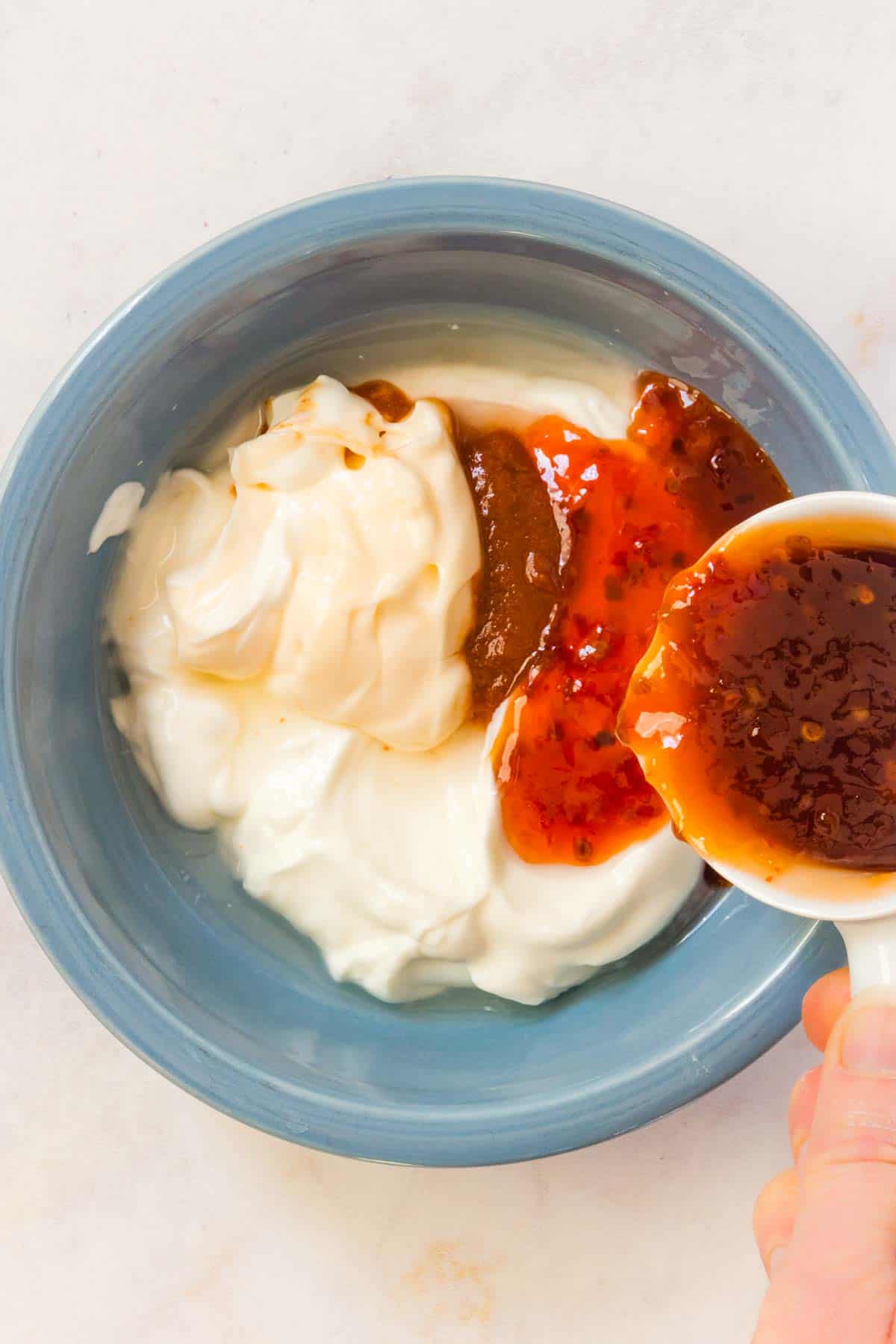 Pouring chili sauce into a blue bowl with Greek yogurt and mayonnaise.