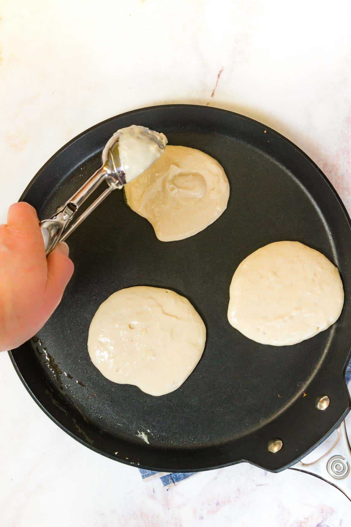 A scoop is used to drop pancake batter onto a hot griddle.