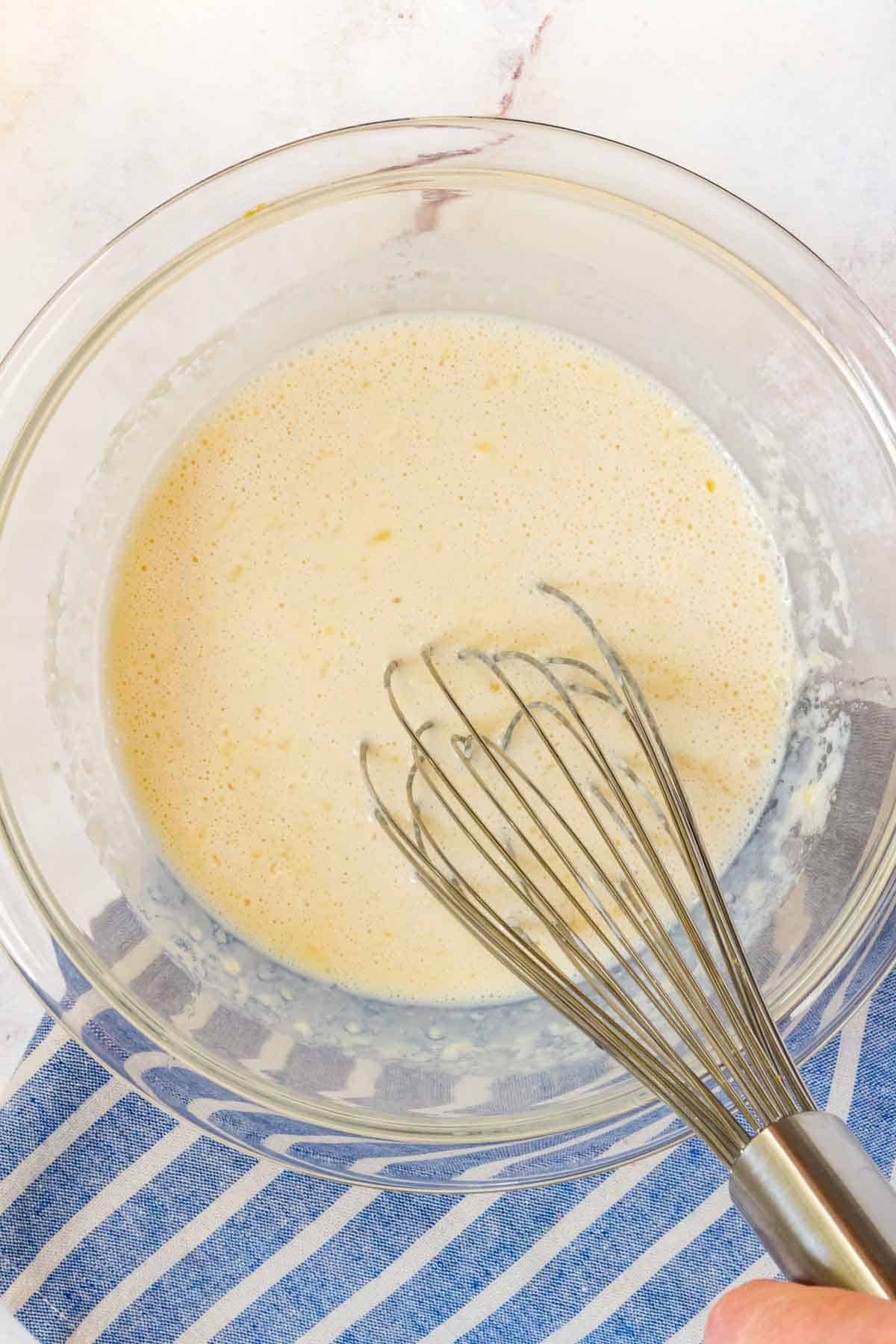 Wet pancake ingredients are whisked together in a glass mixing bowl.