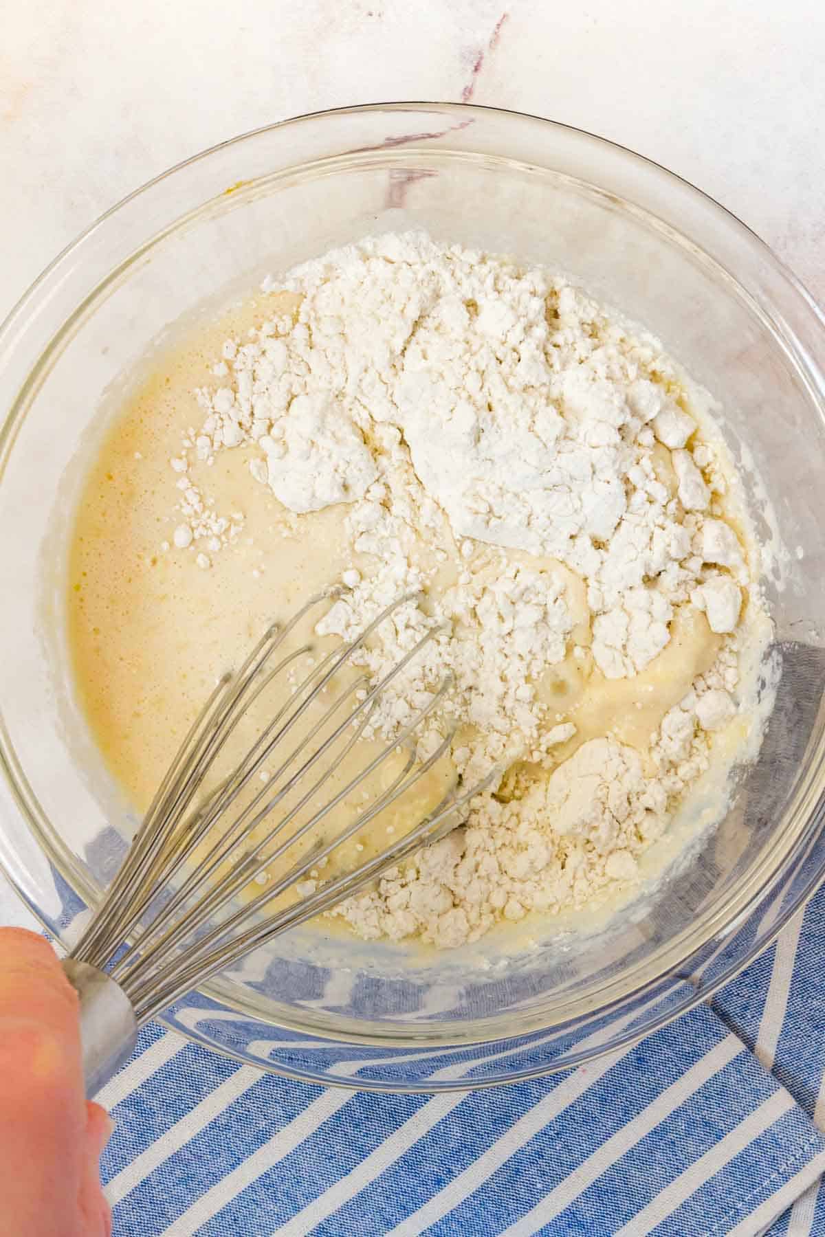 The dry ingredients are whisked together with the wet ingredients in a glass mixing bowl.