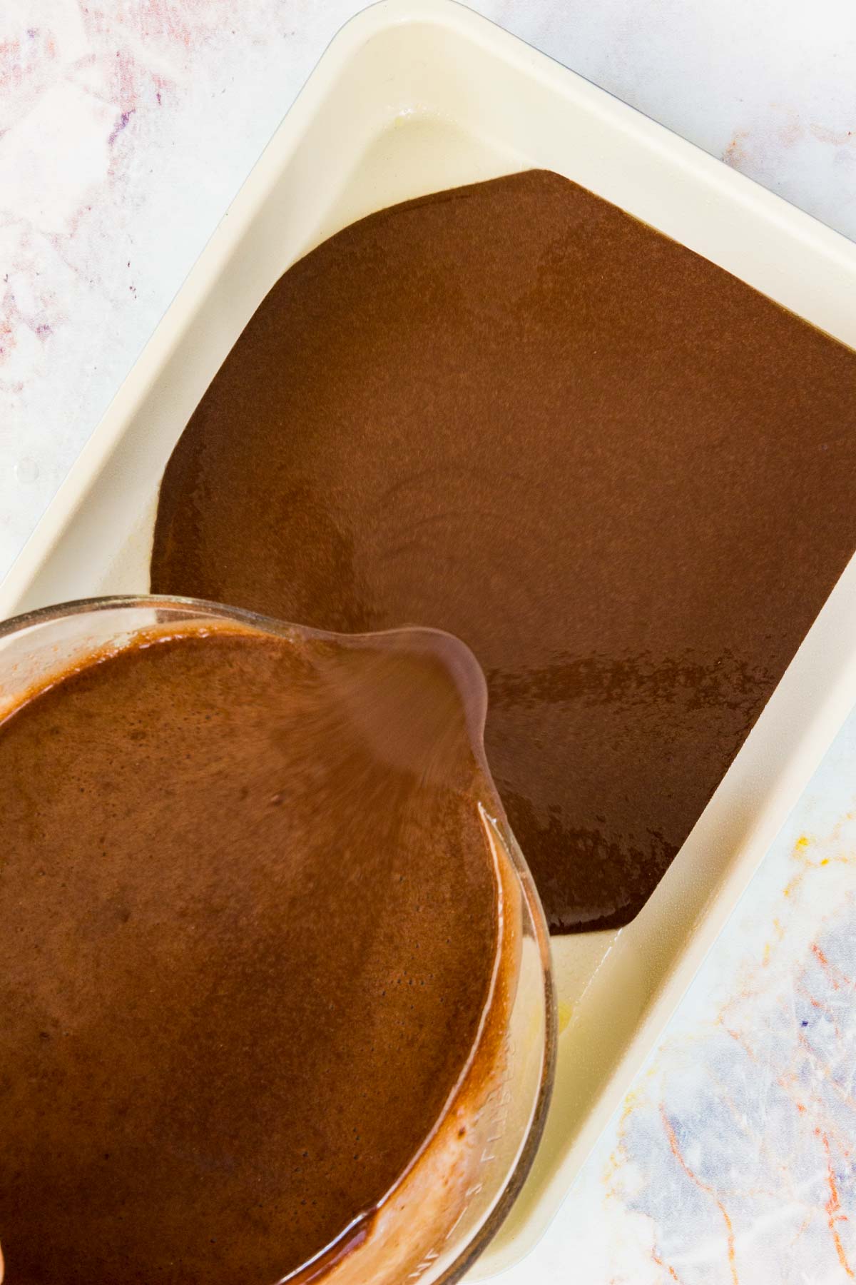Chocolate cake batter is poured into a rectangular baking pan.