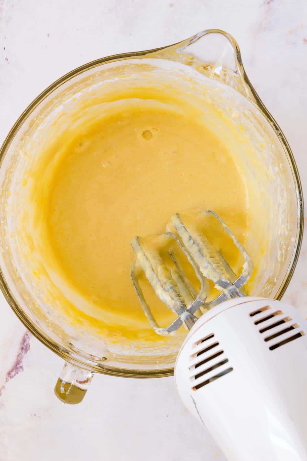 A handheld mixer is used to combine the wet ingredients for cake batter in a mixing bowl.