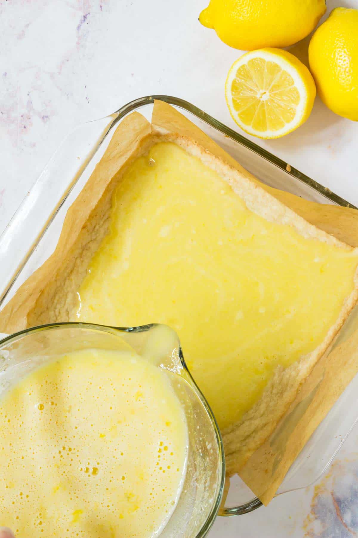 Lemon filling is poured over the shortbread crust in a parchment-lined baking dish.