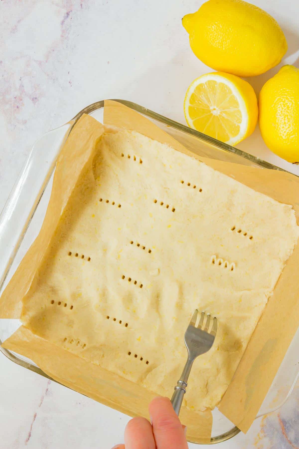 A fork is used to prick holes in the crust dough in a parchment-lined baking dish.