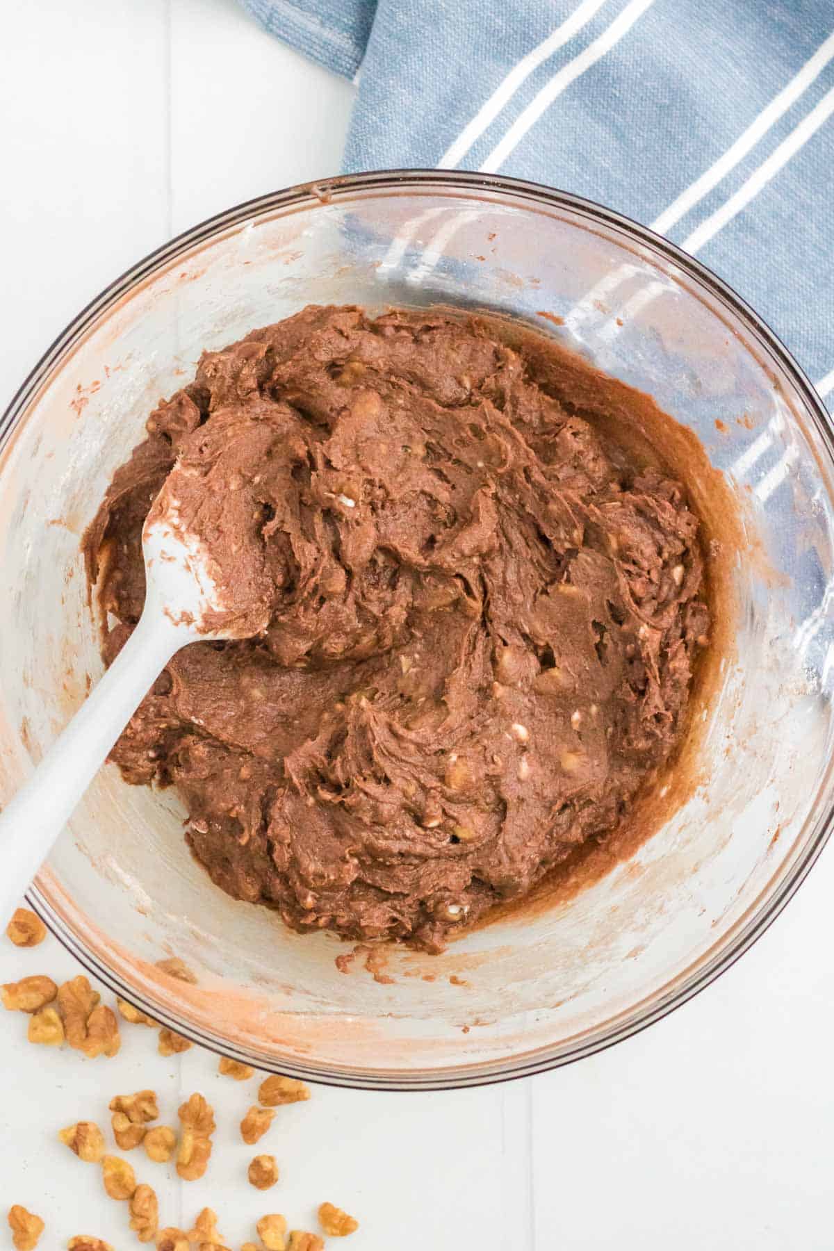 The brownie batter with the walnuts mixed in with a spatula.