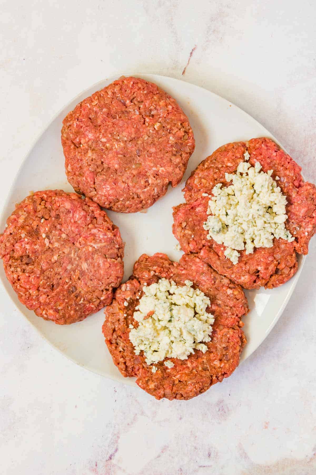 Two fully formed burgers and two with the crumbled blue cheese on the flattened patties.