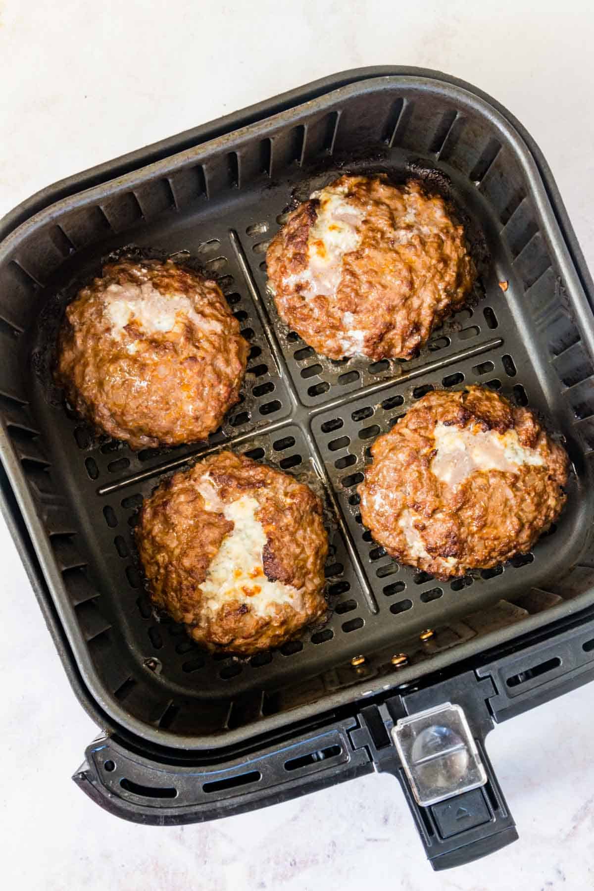 Cooked stuffed blue cheese burgers in an air fryer basket.