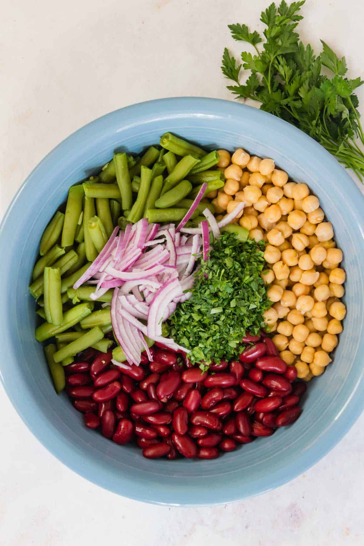 Beans, red onion, chickpeas, and parsley combined in a blue salad bowl.
