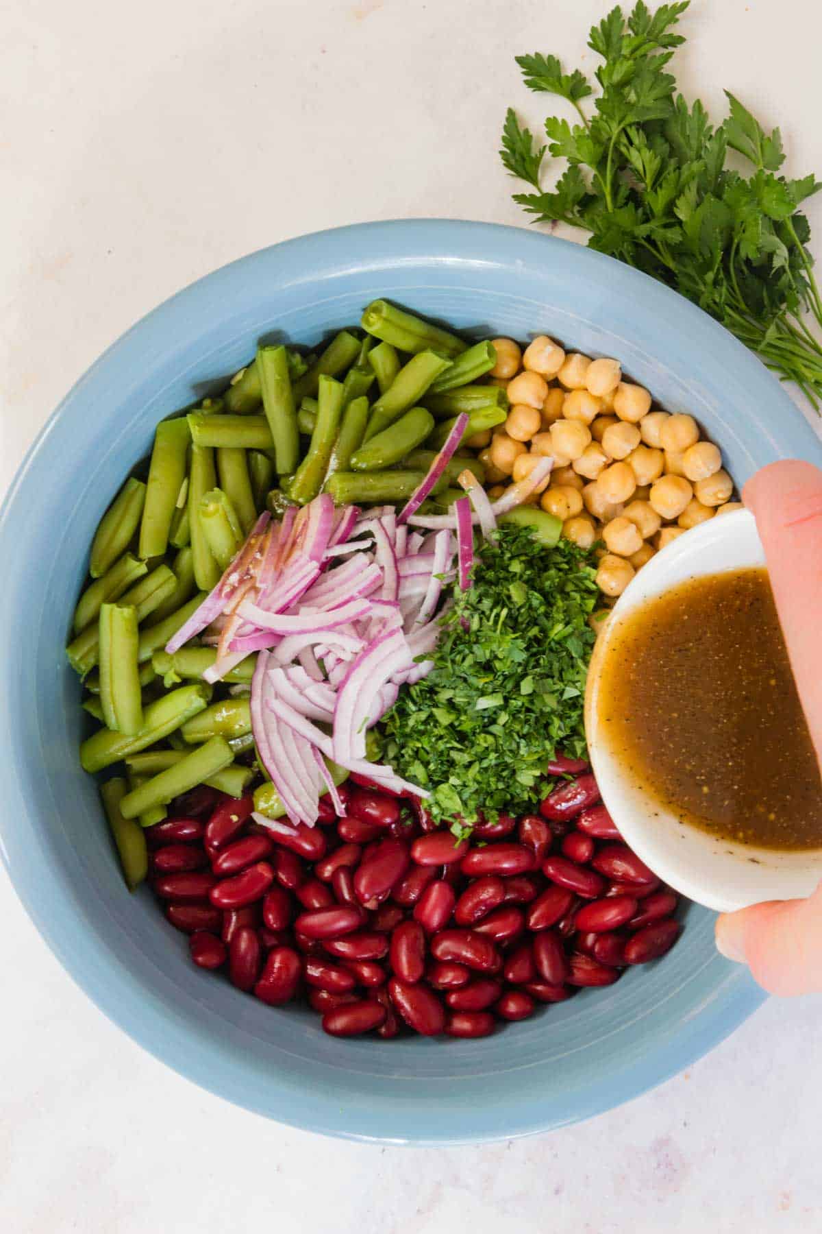 Dressing is poured over a bowl filled with the ingredients for three bean salad.