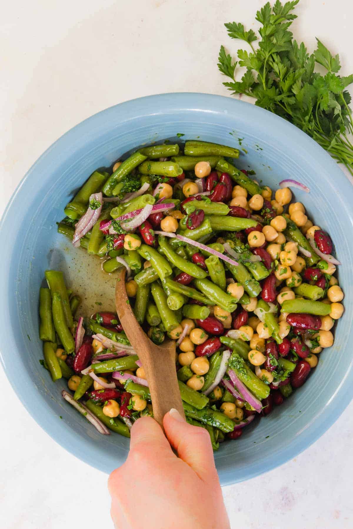 A wooden spoon is used to toss the three bean salad in dressing.