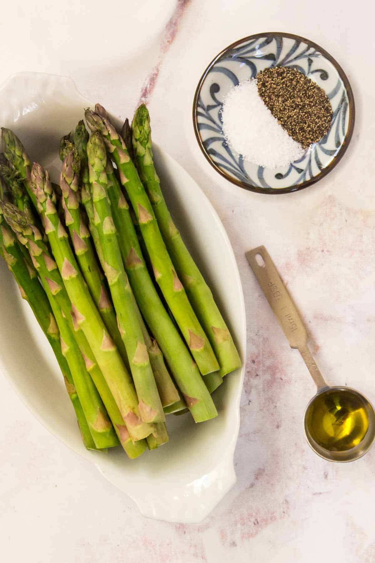 Ingredients to make roasted asparagus on a marble countertop.