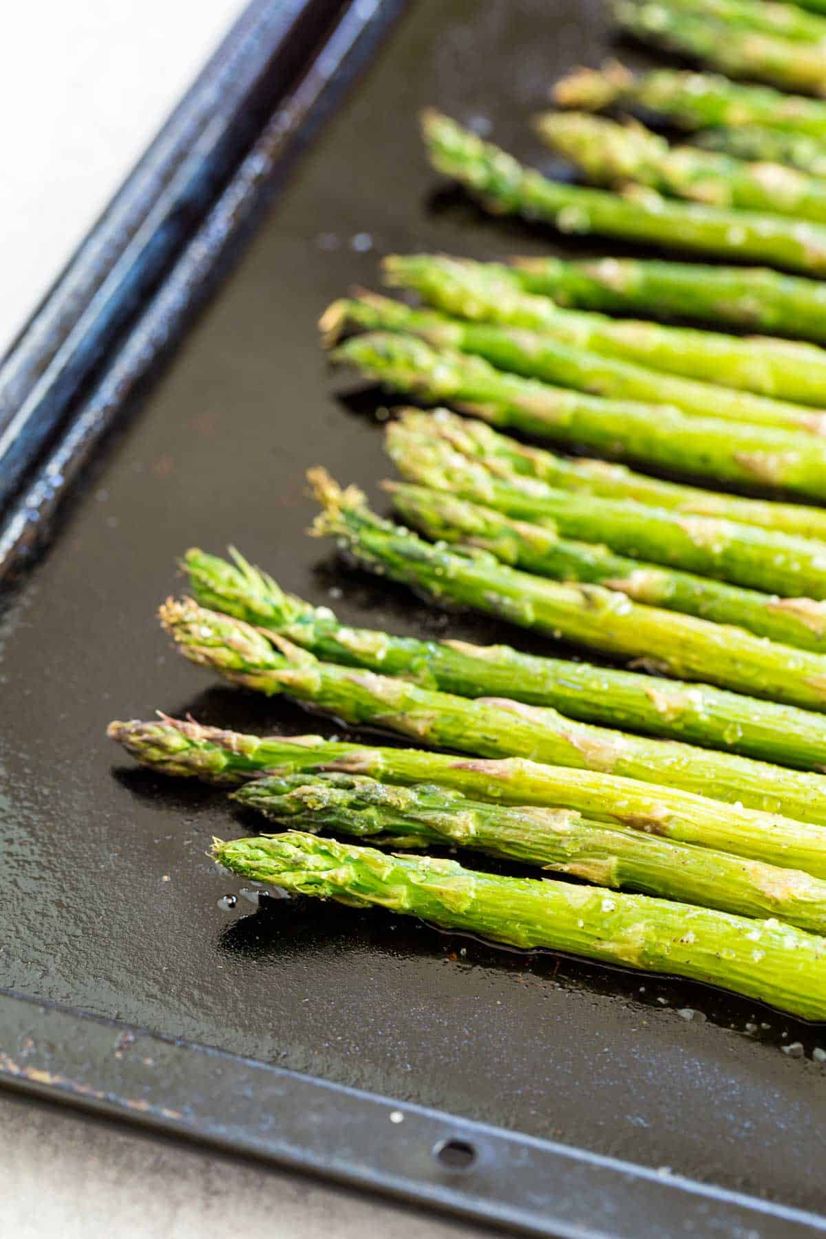 Spears of roasted asparagus on a black oiled baking sheet.